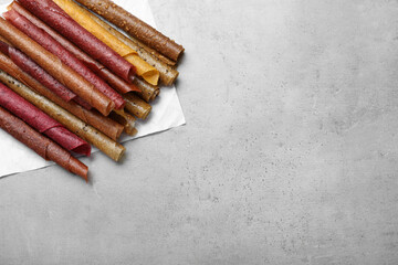 Delicious fruit leather rolls on grey table, flat lay. Space for text
