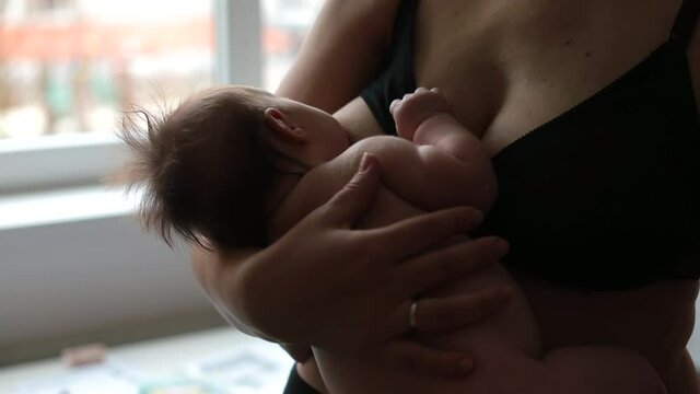 Mom nursing and feeding newborn child in mother's arms. Breastfeeding is an essential way to healthfully nurture and soothe baby. Physical touch and respond to baby's hunger cues. 