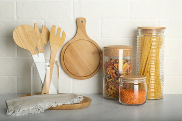 Wooden utensils and different products on grey table near white brick wall in kitchen