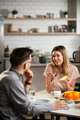 Beautiful woman enjoying in breakfast with her boyfriend. Happy young couple drinking coffee and eating sandwich at home..