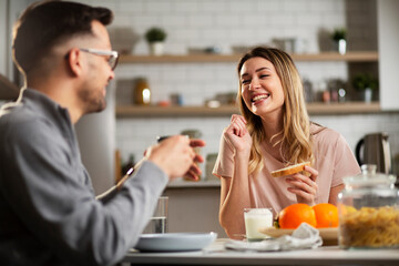 Beautiful woman enjoying in breakfast with her boyfriend. Happy young couple drinking coffee and eating sandwich at home..