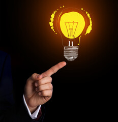 Hand of businessman pointing at glowing light bulb on dark background. Concept of business idea