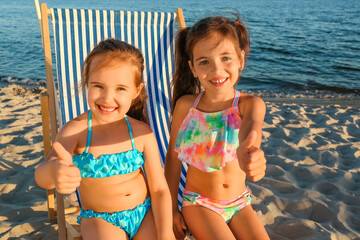 Cute little girls showing thumb-up on sea beach