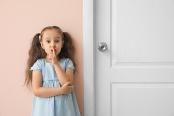 Cute little girl showing silence gesture near closed door