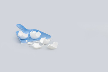 Creative Easter composition with dustpan and broken white eggshells on grey background