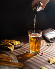 Hand pours light beer into glass, dark background