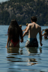 couple entering the water in a lake with people playing in the background