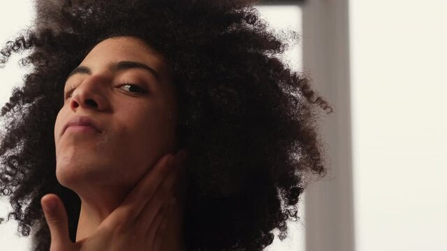 Man facial care. Skin treatment. Moisturizing spf protection. Confident handsome guy with long curly hair applying smearing face cream on light blur background.