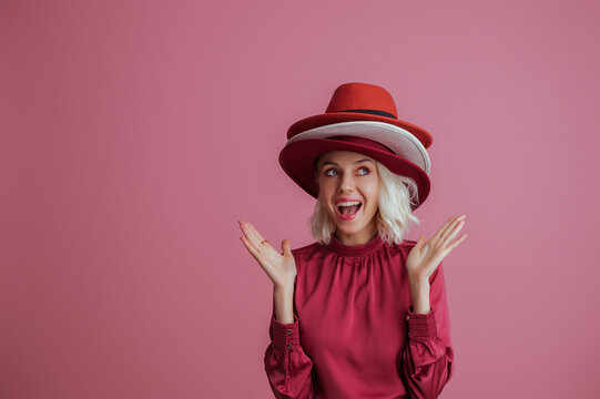 Funny, happy smiling fashionable  woman wearing many hats, posing on pink background. Model looking up. Fashion, sale, shopping advertising conception. Copy, empty space for text