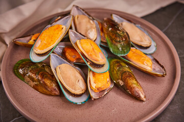 Fresh mussels in the sink sit on a large plate on the dark gray table. The concept of healthy food and fresh seafood and delicacies.