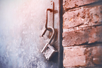 An old metal open lock hangs on the handle of an iron door, standing in a brick building and illuminated by sunlight. An open secret.
