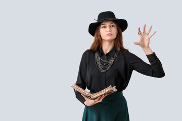 Female fortune teller with spell book on light background
