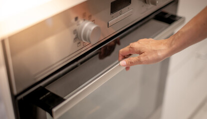 Female hand professional cook opening electric oven, while preparing dinner at home. Hobby, lifestyle. Selective focus. Web Banner.