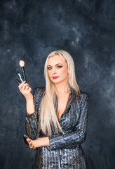 Beautiful female makeup artist holds makeup brushes. A girl on a dark background