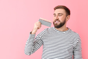 Young man with teeth color chart on pink background