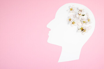 Paper silhouette of a head with natural flowers on a pink background. Top view, place for text.