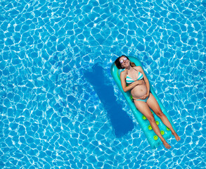 Pregnant woman swim in the pool on matrass