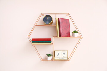 Shelf with books, alarm clock and calendar hanging on color wall
