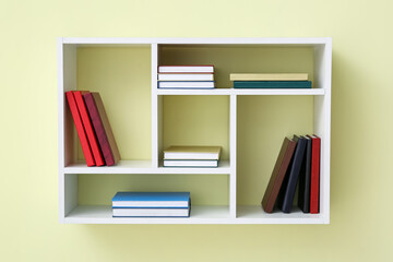 Shelf with books hanging on color wall