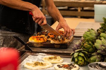 Hands of a man cutting focaccia or pitta bread with toppings.