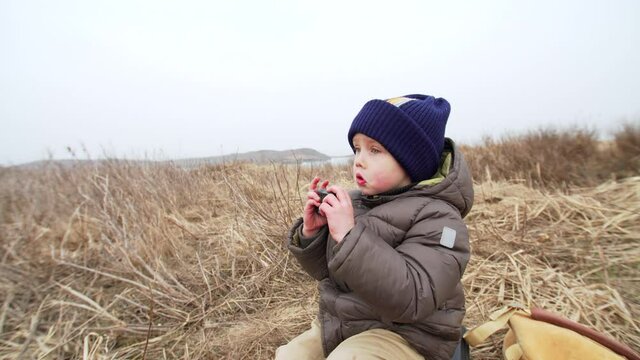 4 years old boy is taking photo of landscapewith action camera and laughting. Spring field with dry grass