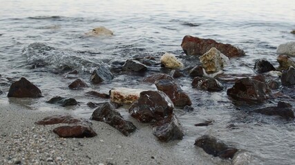 close up of small waves over  rocks on the white sand beach shore