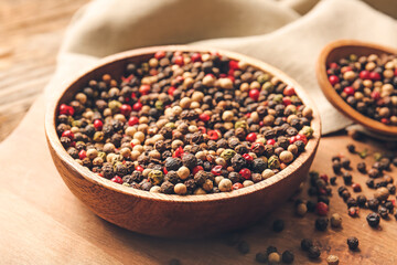 Bowl and spoon with mixed peppercorns on table, closeup
