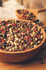 Bowl and spoon with mixed peppercorns on table, closeup