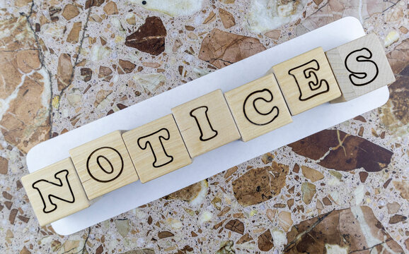 Notices concept with alphabet letters on wooden cubes arranged diagonally on paper over a marble stone background viewed as a flat lay still life