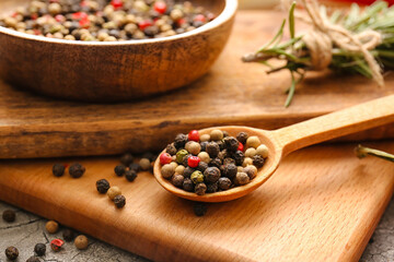 Bowl and spoon with mixed peppercorns on table, closeup