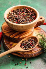 Bowl and spoon with mixed peppercorns on color background