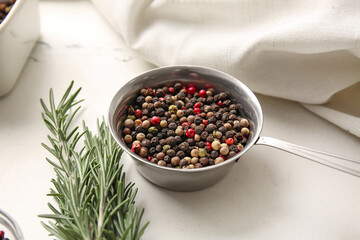 Saucepan with mixed peppercorns and rosemary on light background