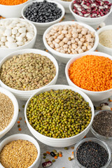 Mix of legumes, chickpeas, lentils, beans, peas, quinoa, sesame, chia, flax seeds in bowls on a gray concrete background. Healthy, vegan and gluten free food.