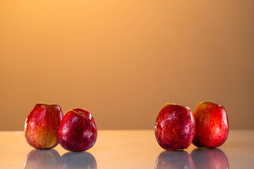 Red apples are on the table. reflective surface, yellow background. sunset. summer mood. nice weather. healthy lifestyle. vitamins