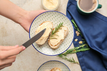 Woman spreading butter onto slice of fresh bread on light background