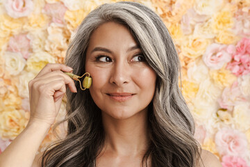 Mature woman massaging face with jade roller standing