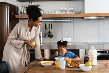 Happy black mother and daughter having breakfast at home kitchen