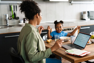 Fototapeta premium Black woman working while having breakfast and playing with her daughter