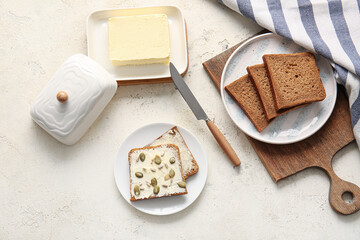 Slices of fresh bread, butter and seeds on light background