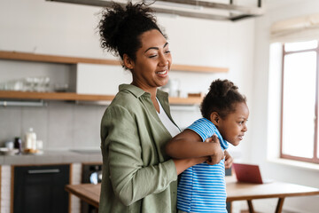 Obraz premium Black happy mother and daughter laughing and playing at home kitchen