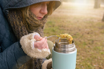 Woman is eating a warm meal from a thermos