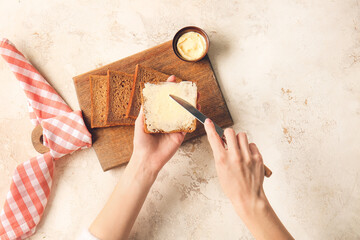Woman spreading butter onto slice of fresh bread on light background