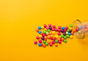 colorful candies poured from a glass jar on a colored background