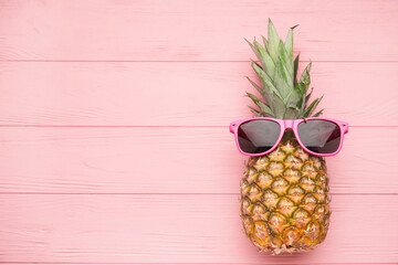 Pineapple with sunglasses on color wooden background