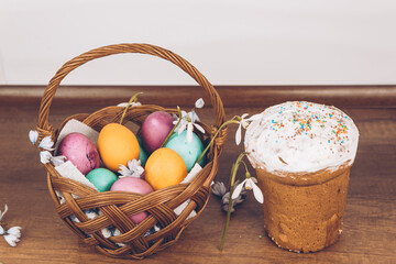 On a wooden table is an Easter basket with yellow, green and purple eggs, decorated with...