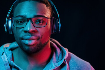 With headphones. Futuristic neon lighting. Young african american man in the studio