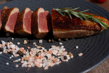 Grilled Duck Breast Slices. Served on the dark plate, wooden table background