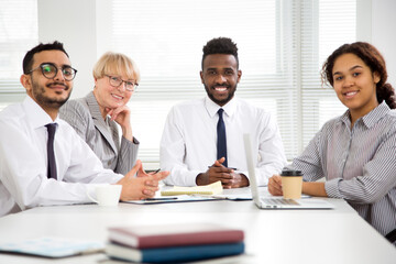 Multy-ethnic group of business people working while sitting at the office desk and smiling at camera