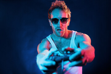 Having fun. Neon lighting. Young european man is in the dark studio