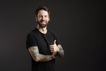 Bearded brunette man with tattoo smiling and showing thumb up